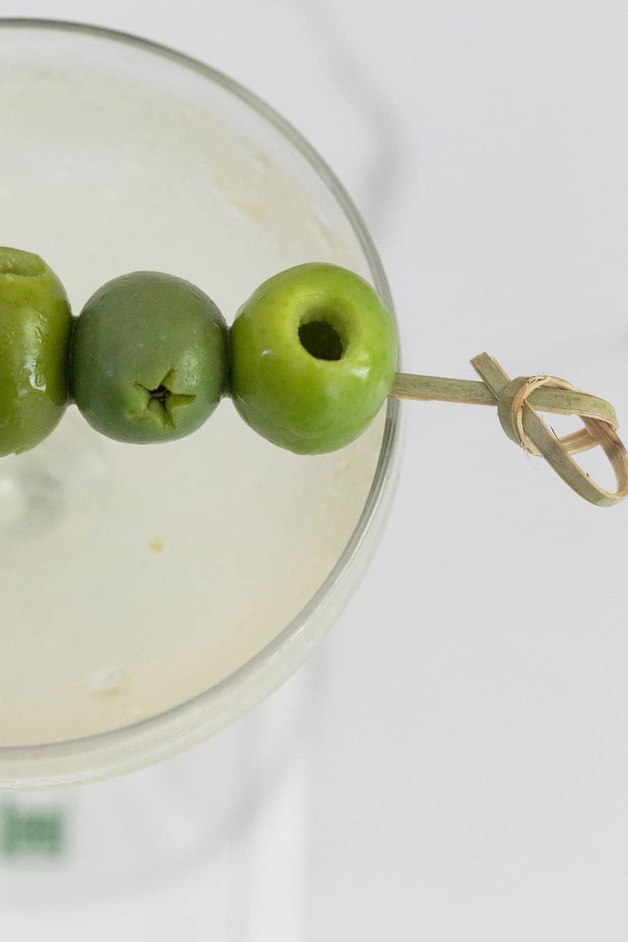 Green olives on a pick laying over a dirty martini.