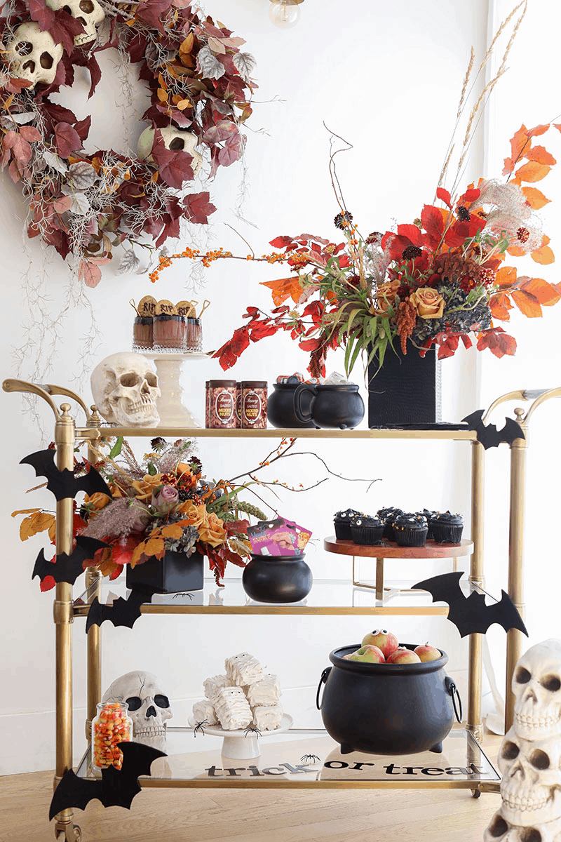 Halloween bar cart with cauldrons, flowers, skulls and desserts.