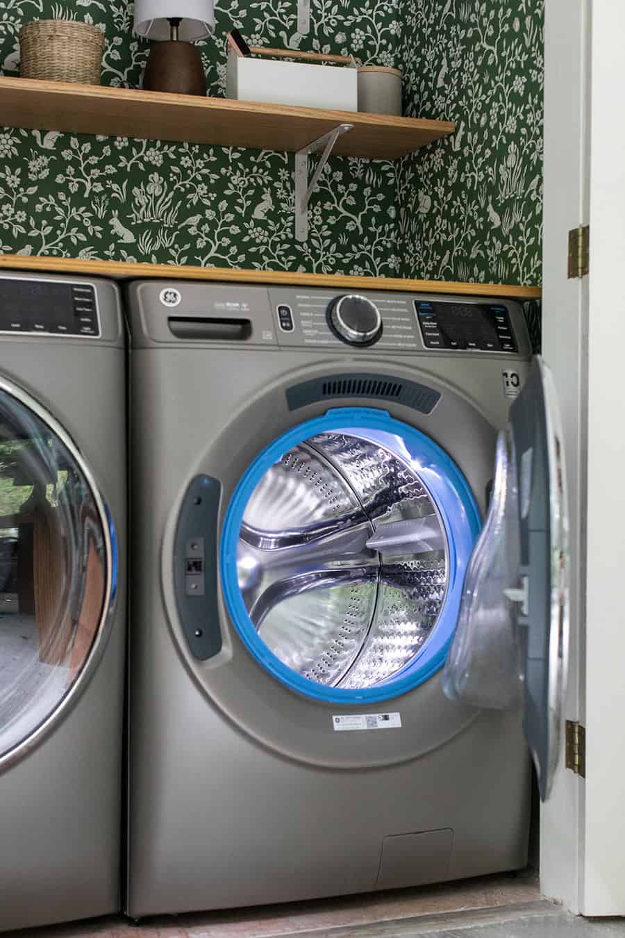 GE washer and dryer with the door open in a laundry closet with green wallpaper.