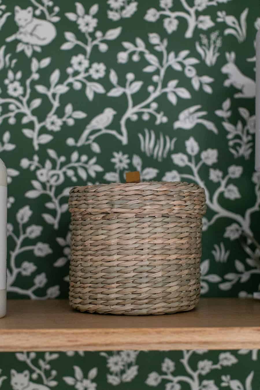 Woven basket on an oak shelf with green wallpaper.