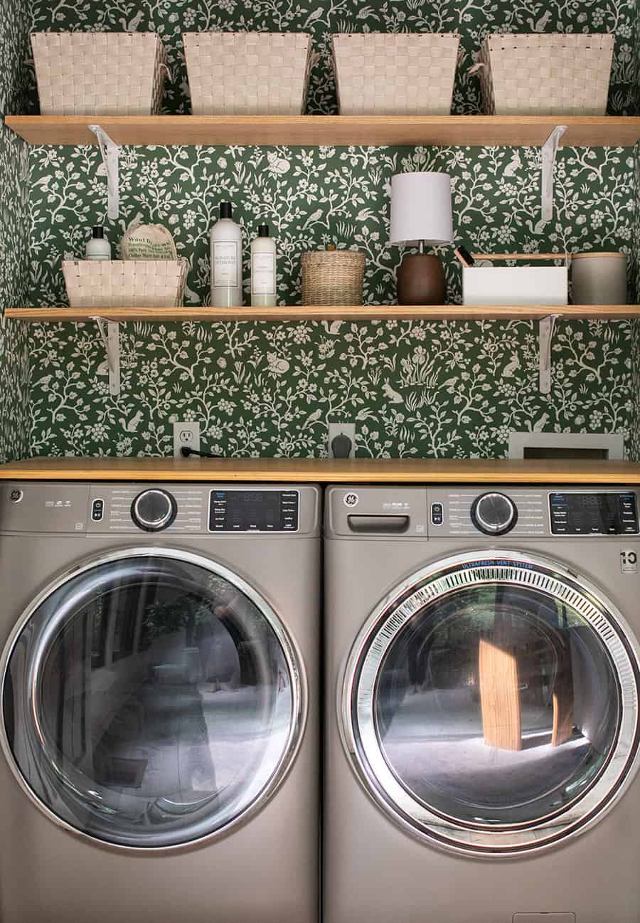 Laundry closet with woodsy green wallpaper, baskets and open shelving.