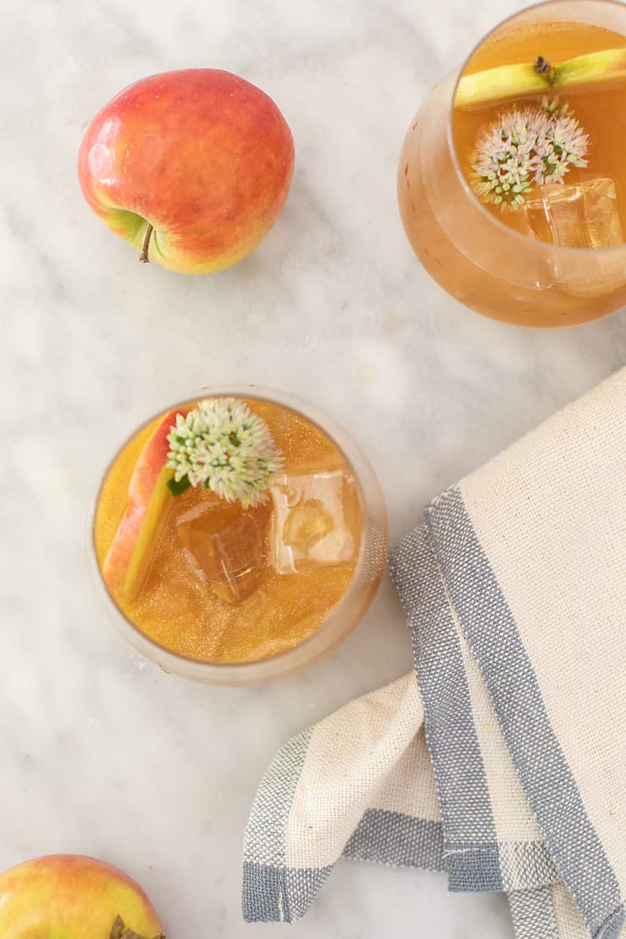 Golden cocktail in a glass with shimmer, apple and a napkin on a marble table - poison apple halloween cocktail, easy cocktail halloween season, sour apple