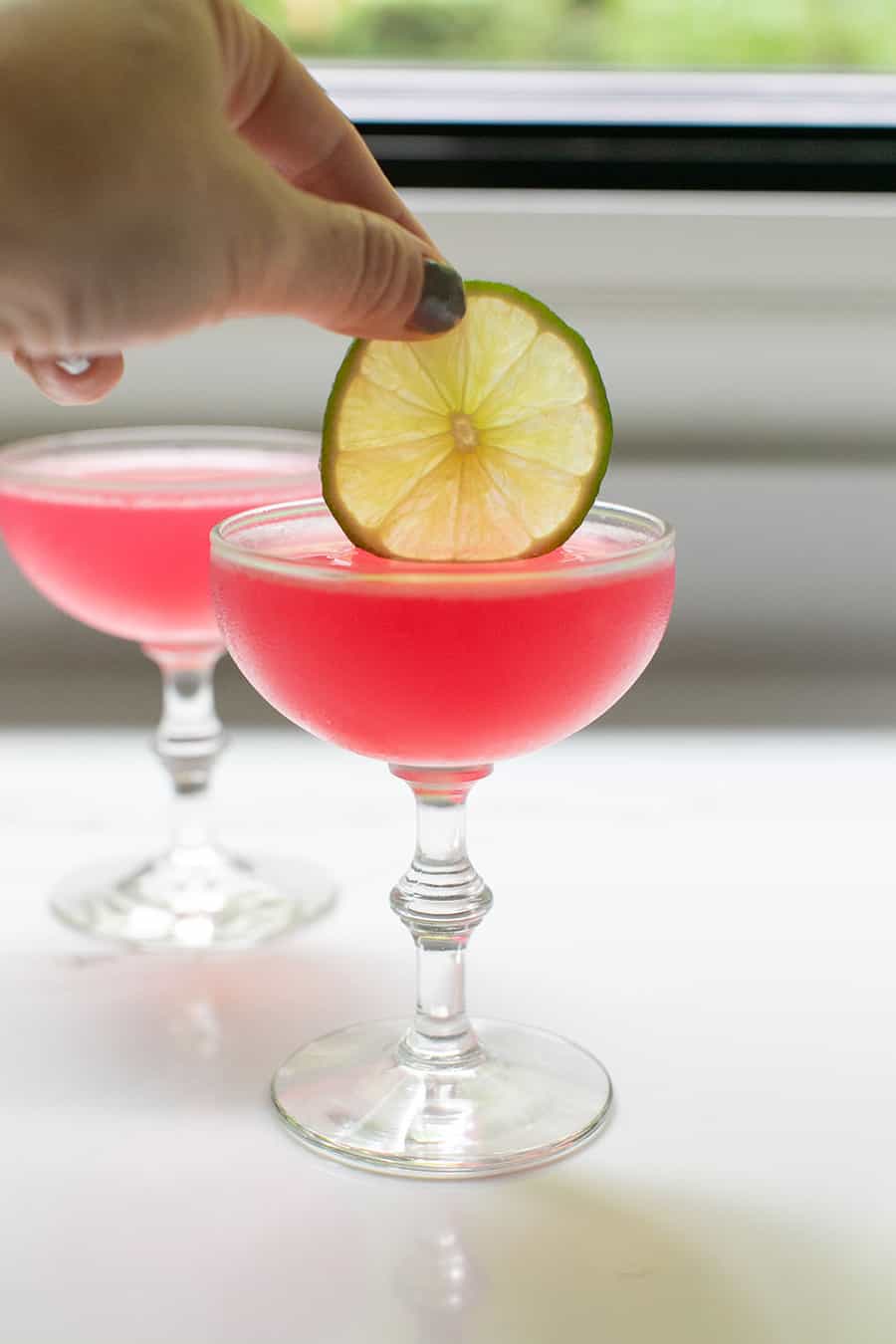 Adding a lime wedge into a pink cosmopolitan cocktail recipe. - vodka cointreau cranberry juice