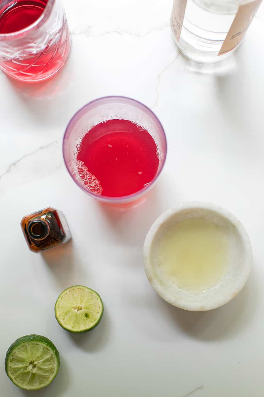 Lime juice, pink cocktail in a shaker and a bottle of vodka. - chilled cocktail glass