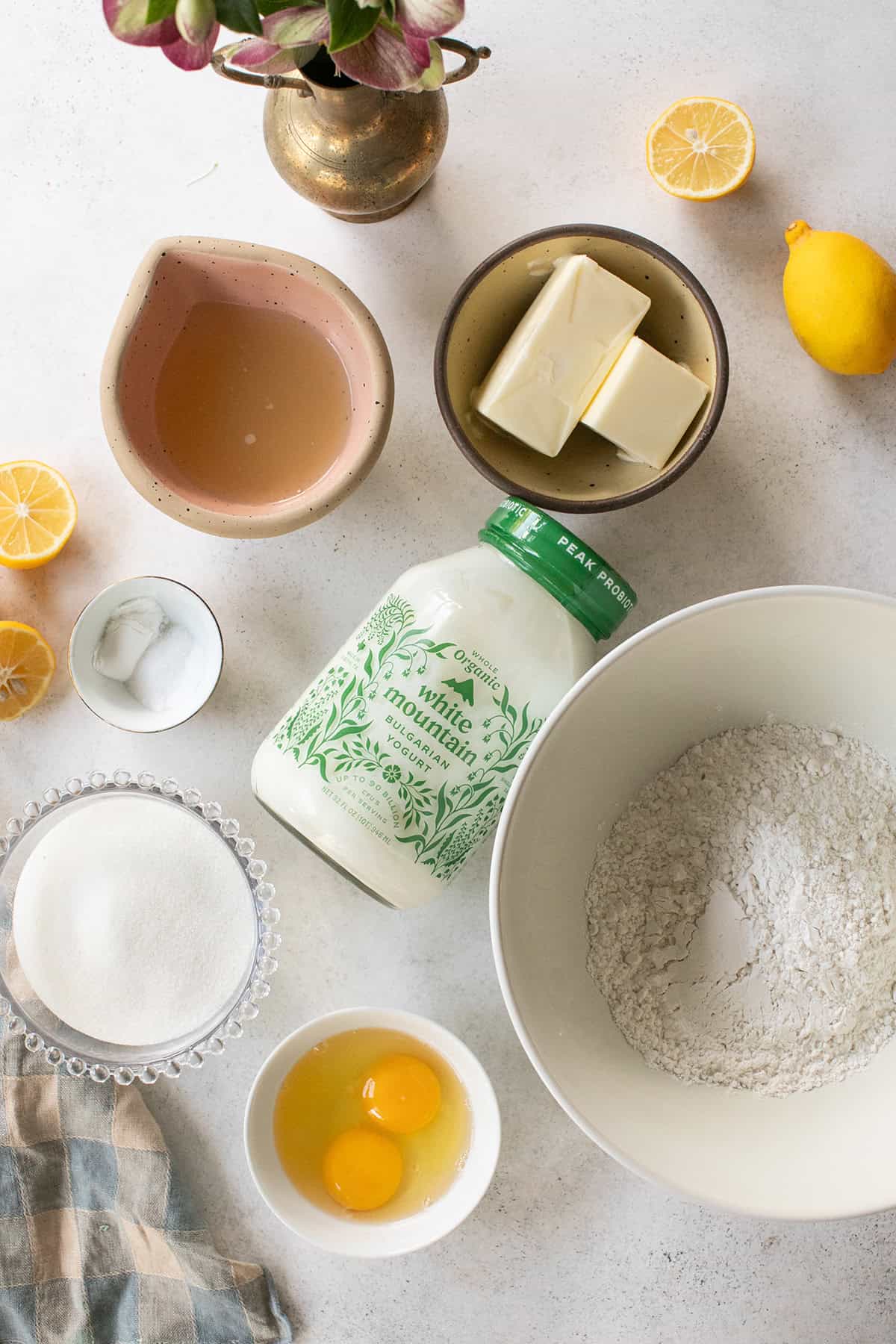 Ingredients to make a lemon loaf cake with cake flour, yogurt, butter, eggs and lemon juice.