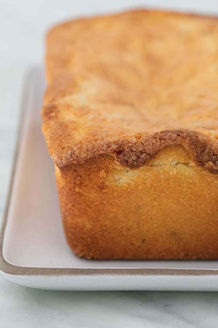 Golden brown rosemary lemon loaf cake on a white Heath ceramics platter.