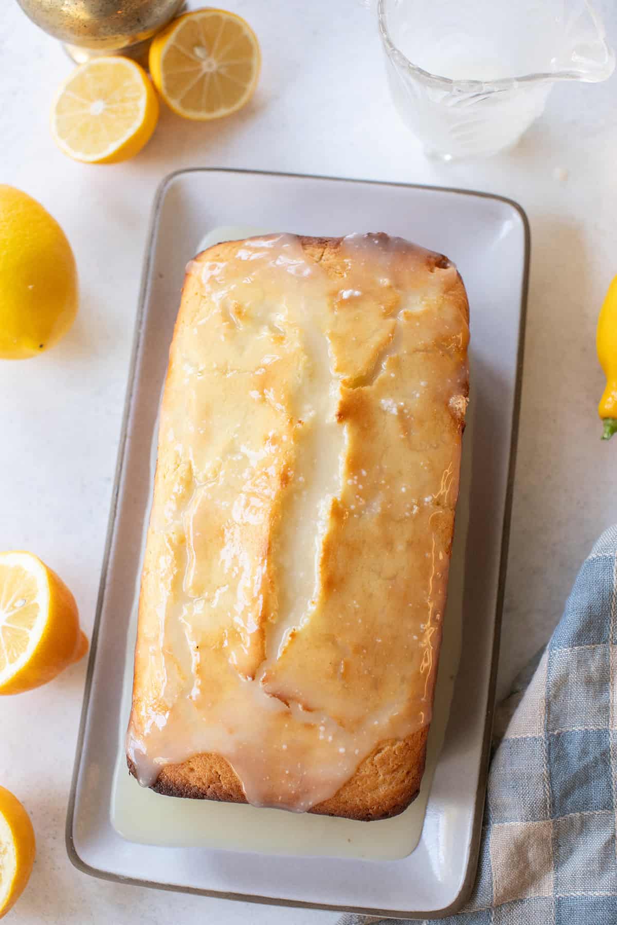 Bright and zesty lemon glazed pound cake on a white plate, surrounded by fresh lemons and a glass of glaze.