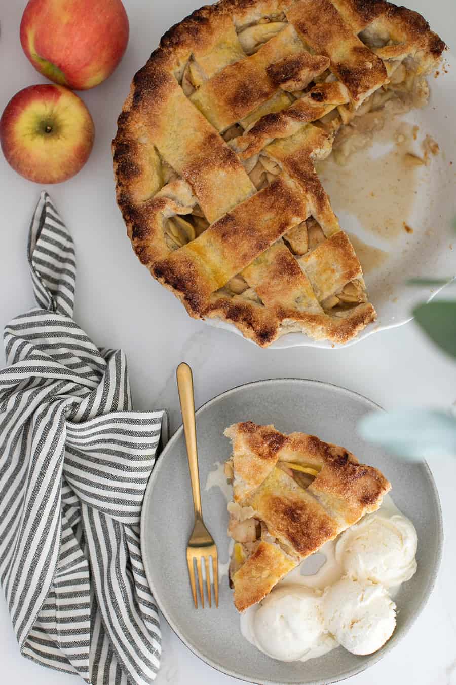 Apple pie with a slice taken out of it on a counter with napkin and apple