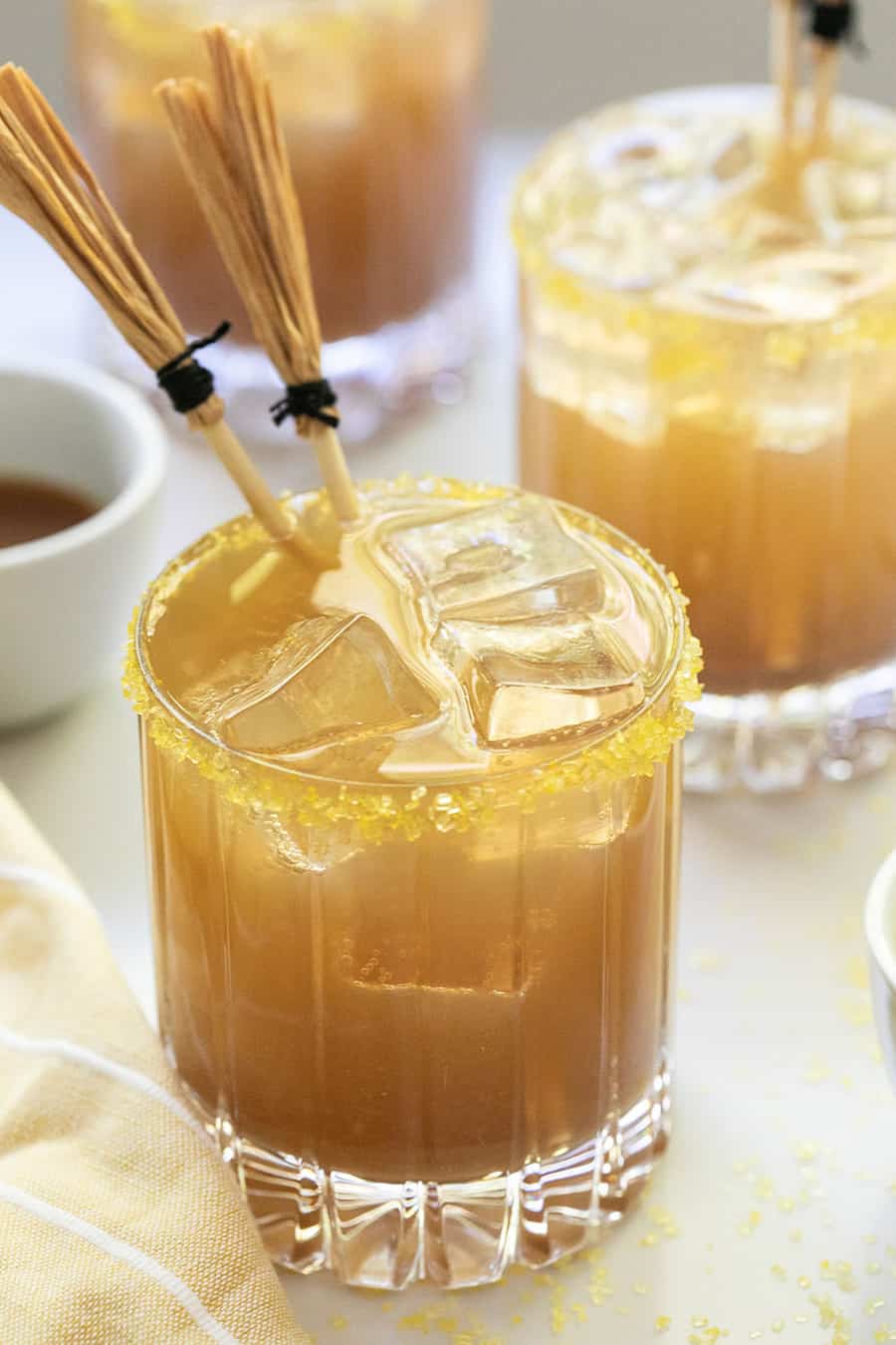 Butterbeer in a glass with ice, sprinkles and broom stick stirrers. 