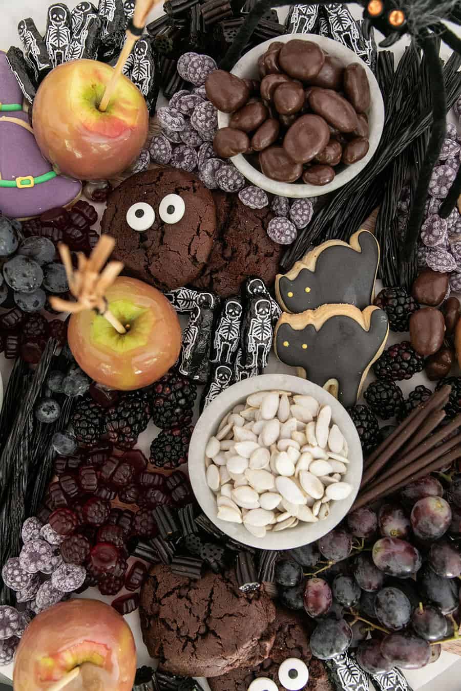 A Halloween dessert platter filled with caramel apples, fruit, chocolates and cookies.