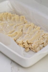 Shortbread being pressed into a baking dish.