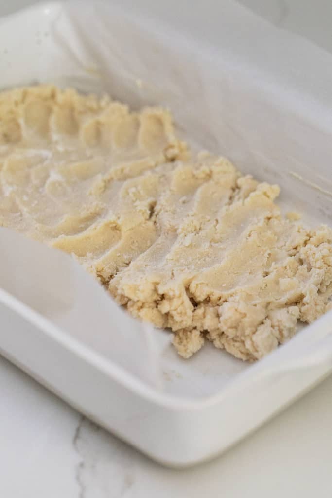 Shortbread being pressed into a baking dish.