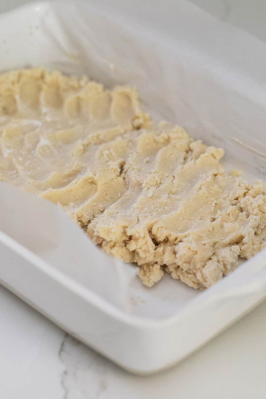 shortbread dough being pushed into a baking dish.