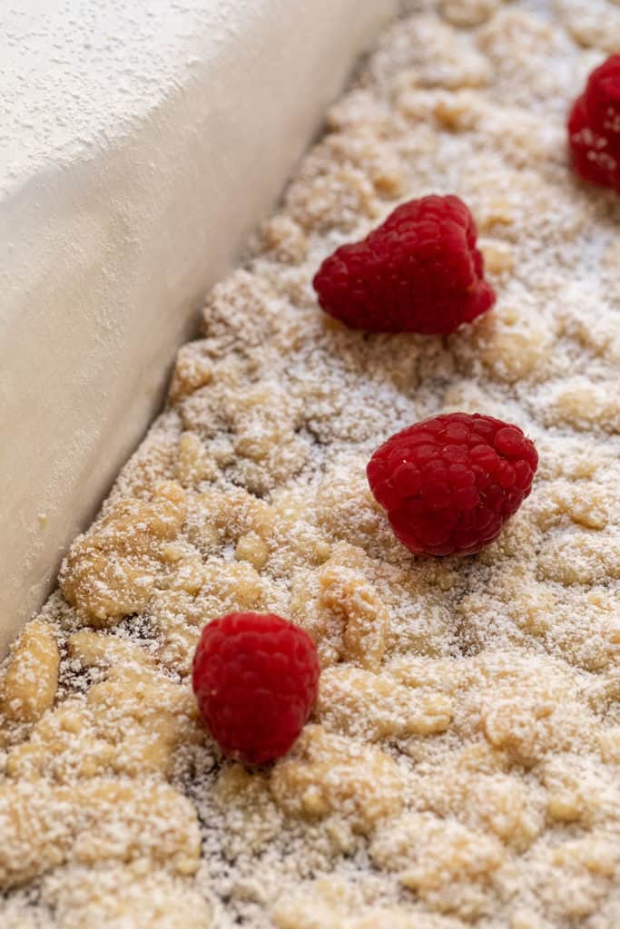 Shortbread cookie bars before cutting, topped with powdered sugar and fresh raspberries.