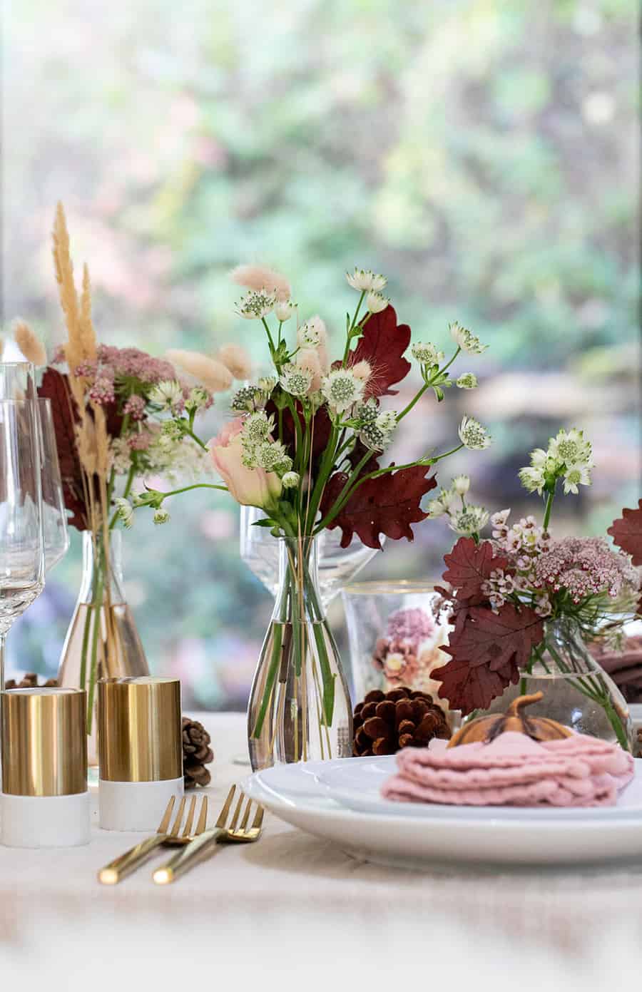 Bud vases with flowers, salt and pepper shaker and gold flatware.