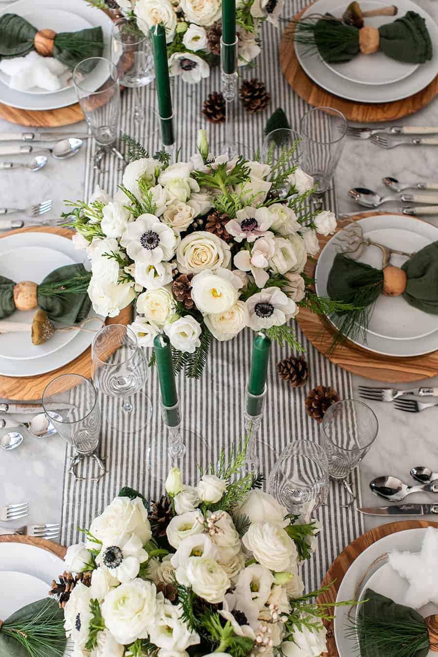 Christmas table decorations like flowers, candles, chargers and plates on a table.