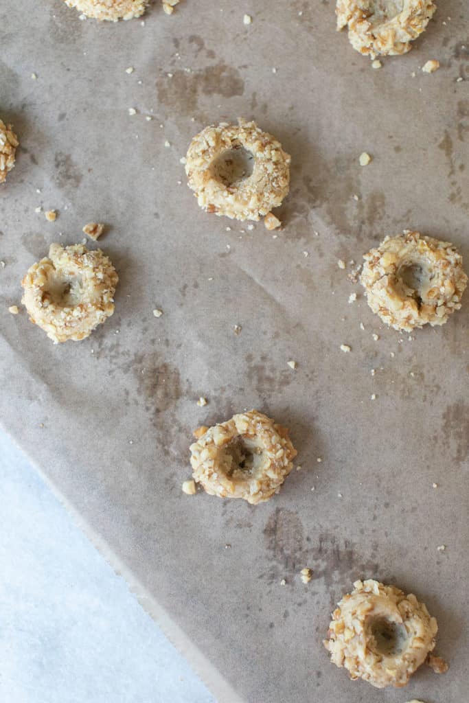 Thumb print cookies on a baking sheet lined with parchment paper before baking.