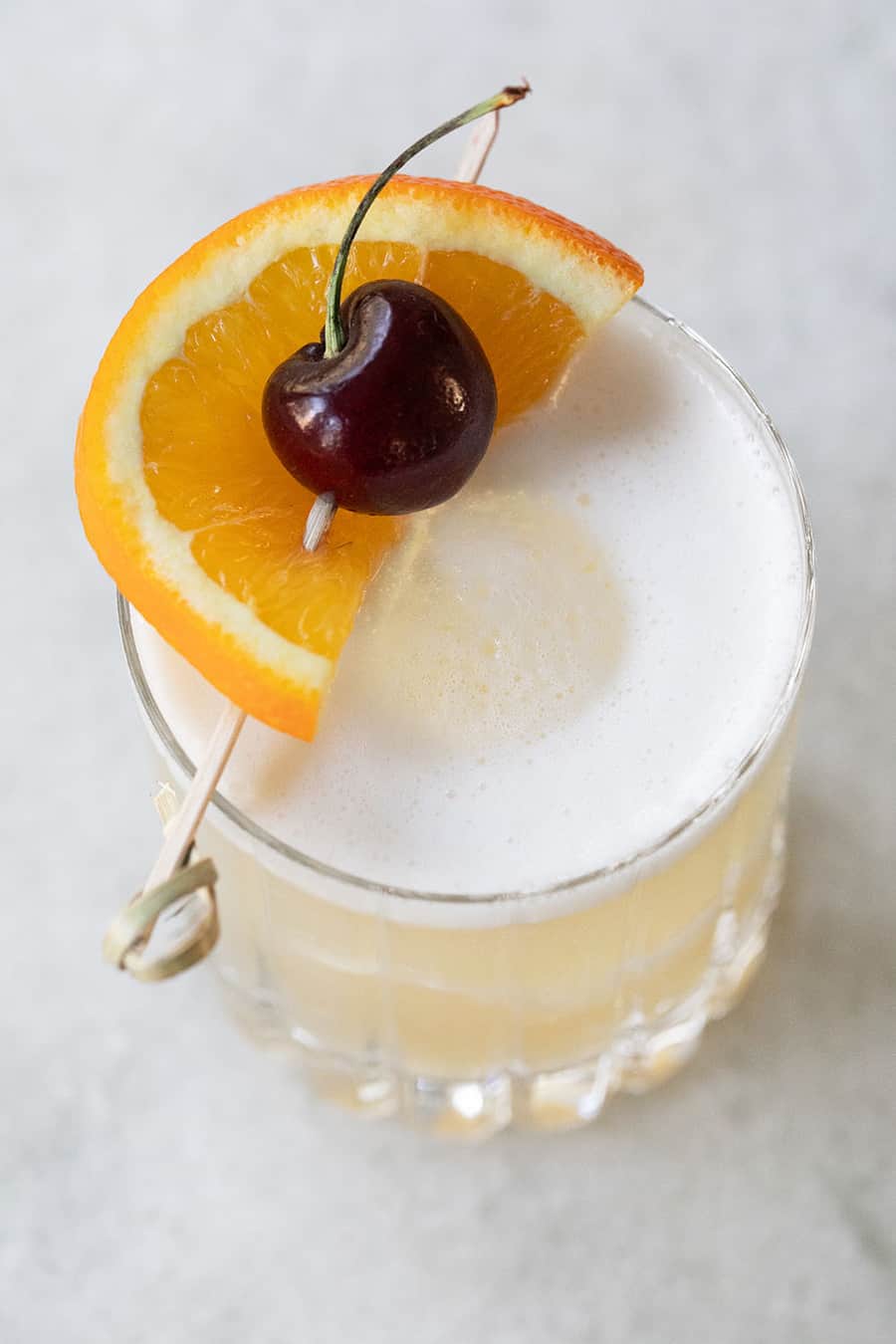 Whiskey sour with an orange slice and fresh cherry on top.