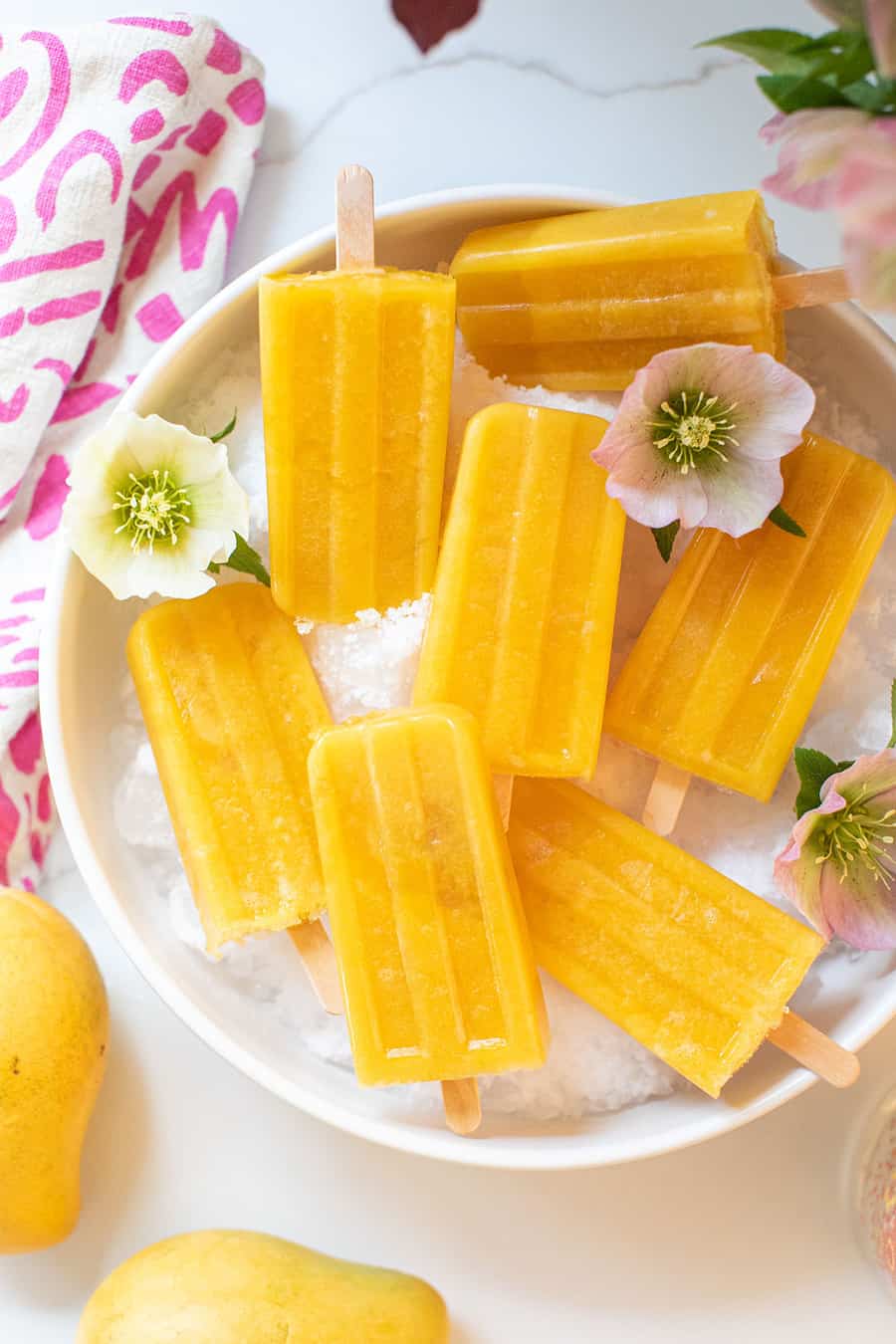 Mango popsicle recipe in a bowl with pretty flowers.