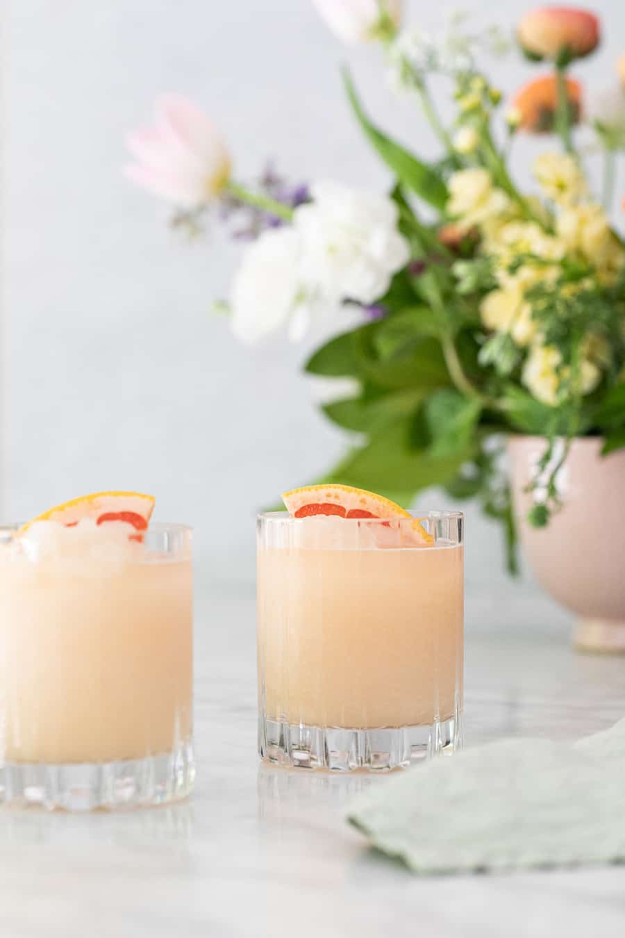 Paloma cocktail frozen in a glass with flowers in the back