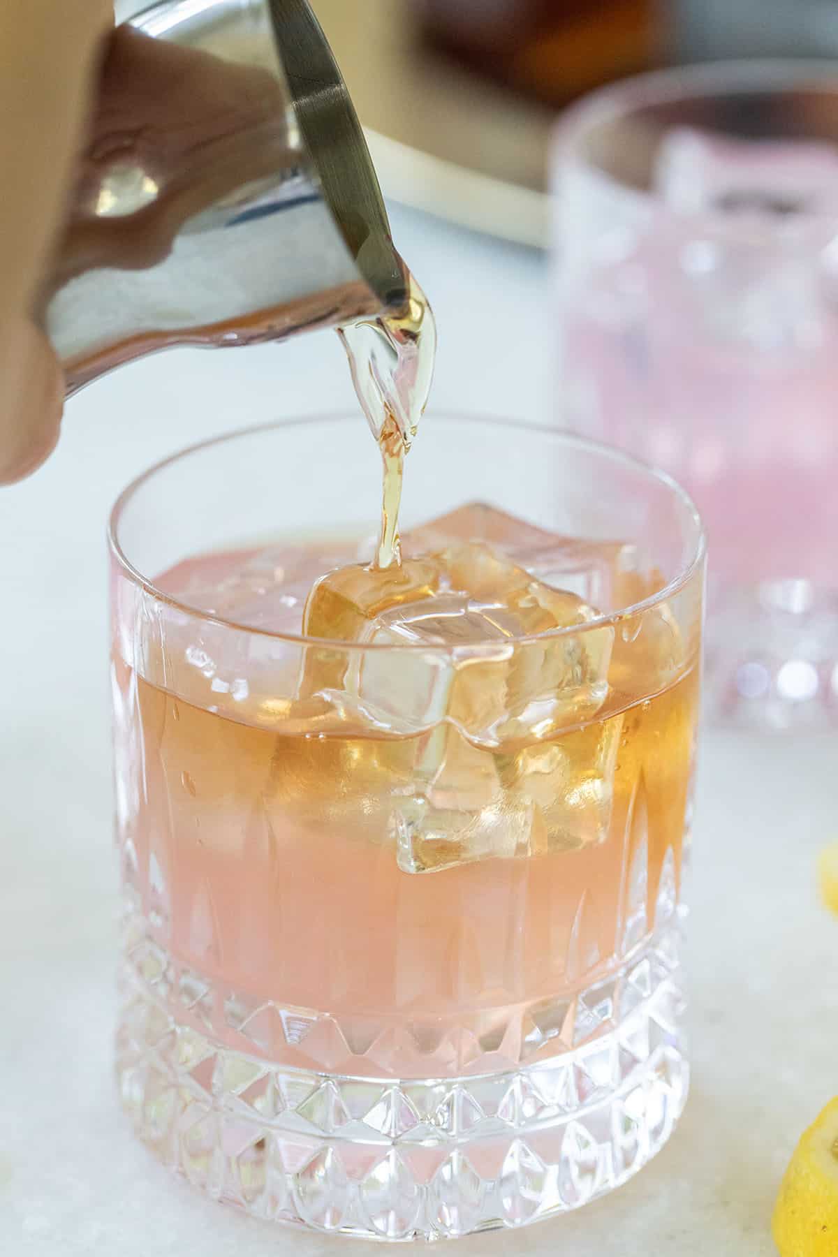 Brown spirit being poured over ice in a cocktail glass.