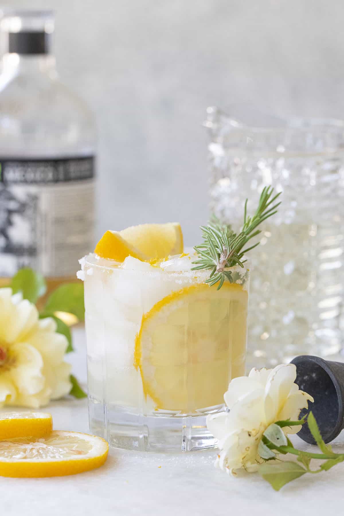 Lemon margarita in a glass with lemon slices and rosemary for garnish. 