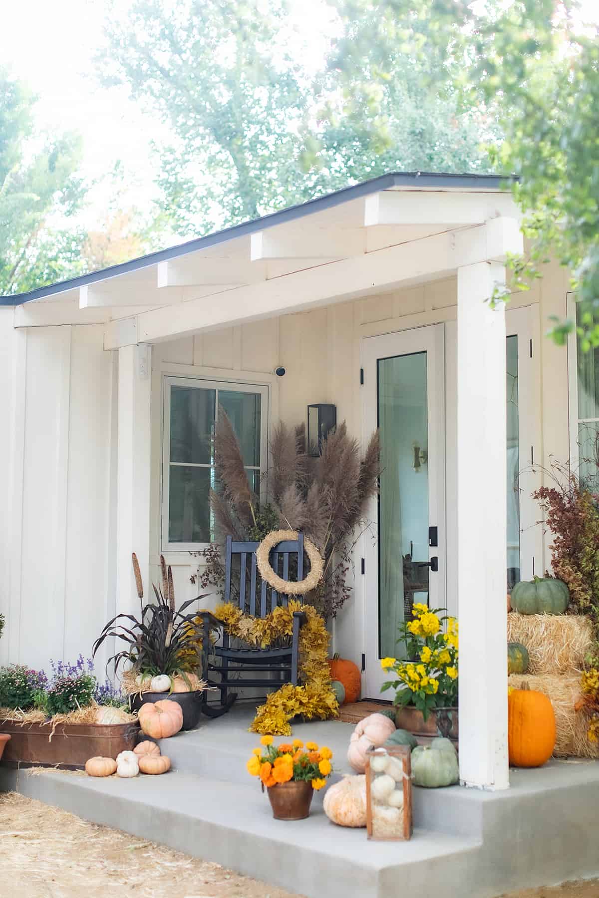 A charming front porch decorated for fall with pumpkins, flowers, and wreaths.