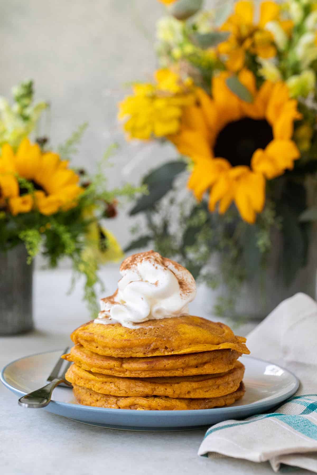 A pumpkin pancake stack with whipped cream and cinnamon.