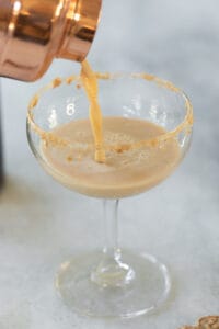 pouring a gingerbread cocktail into a martini glass