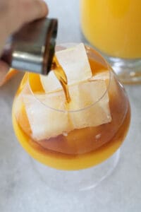 pouring rum over orange juice in a glass
