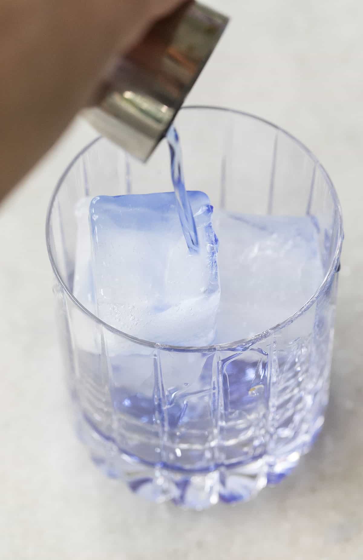 pouring blue gin into a glass filled with ice