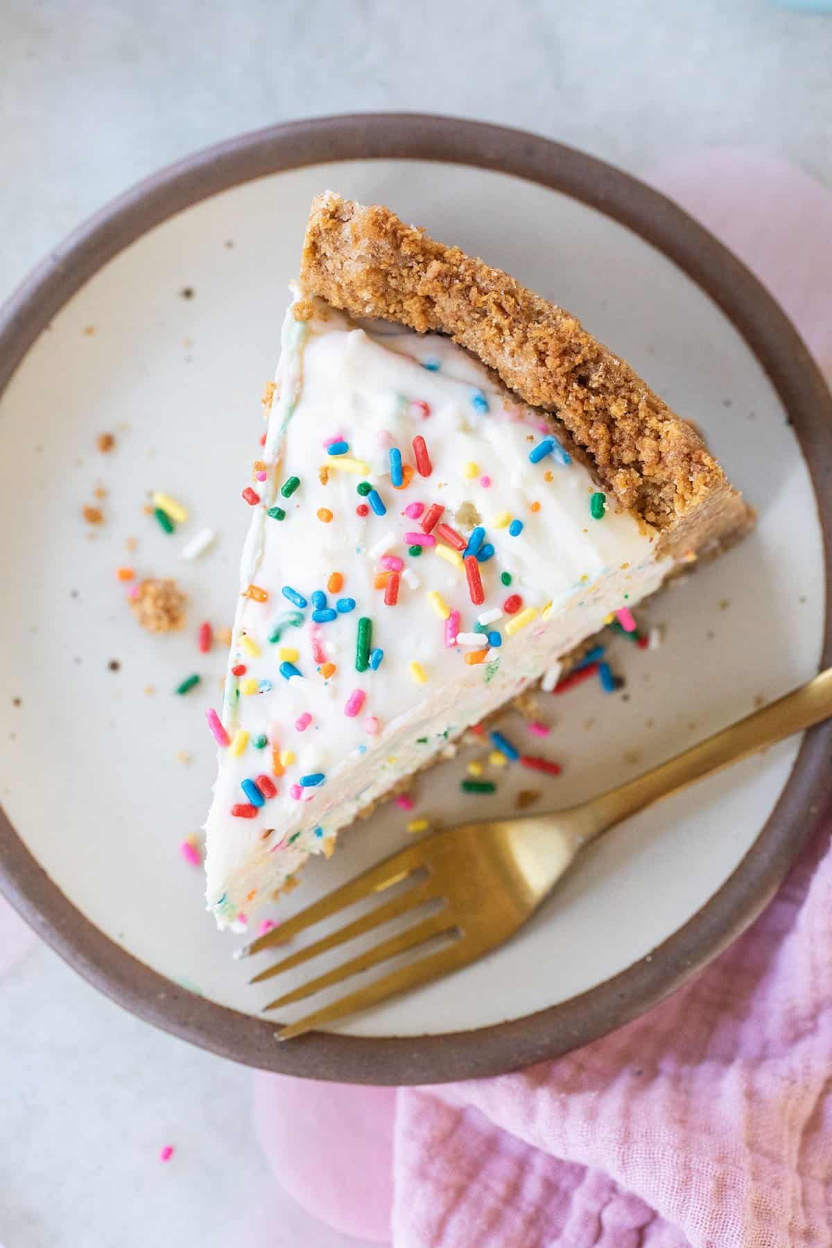 birthday cheesecake with sprinkles and a gold fork.