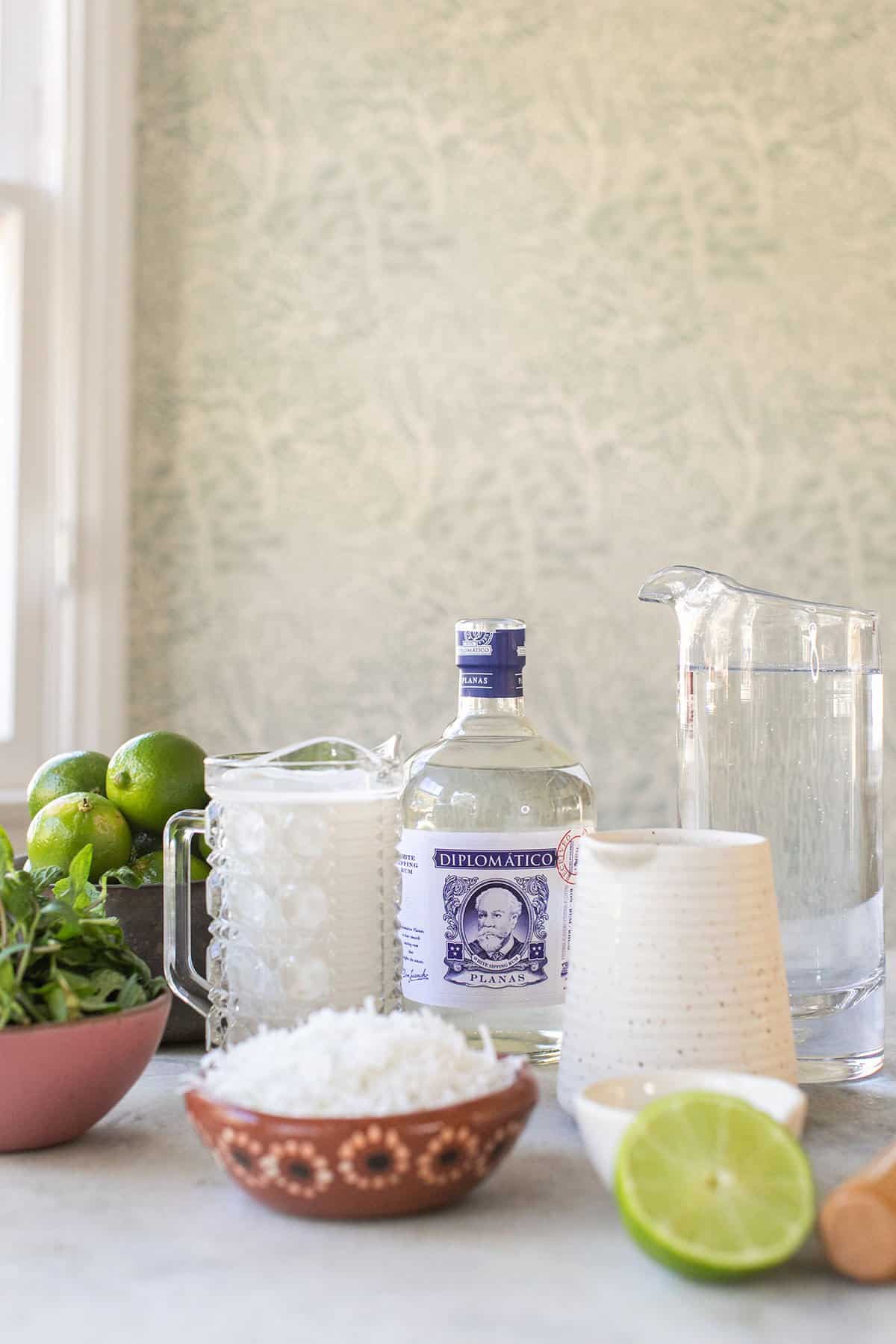 Rum, shredded coconut, lime, coconut cream, mint, sparkling water on a table.