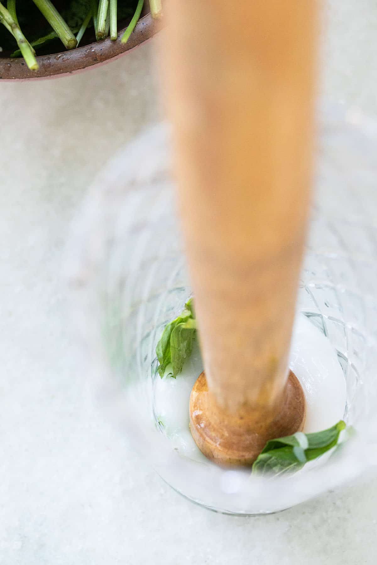 Muddling coconut cream and mint together in a glass.