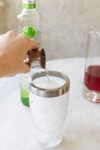 pouring apple vodka into a cocktail shaker