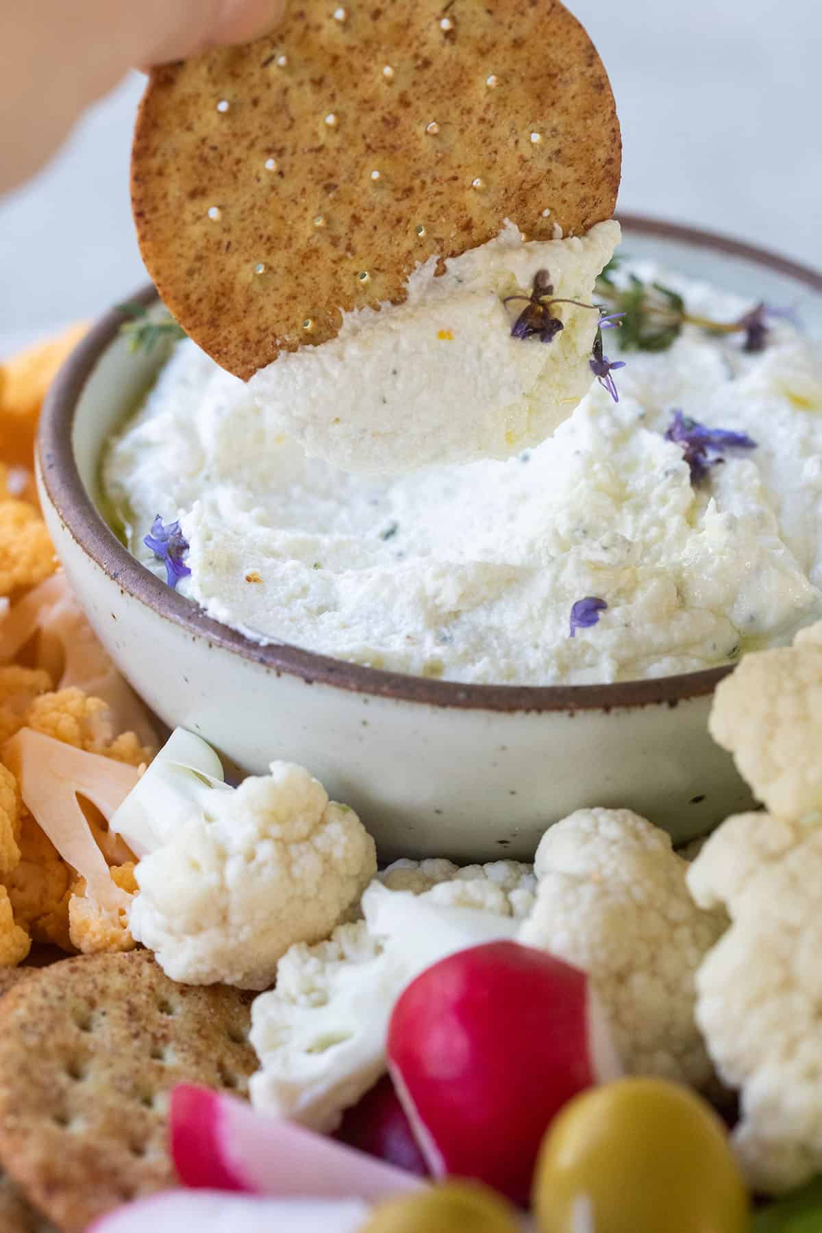 Cracker being dipped into creamy whipped goat cheese.