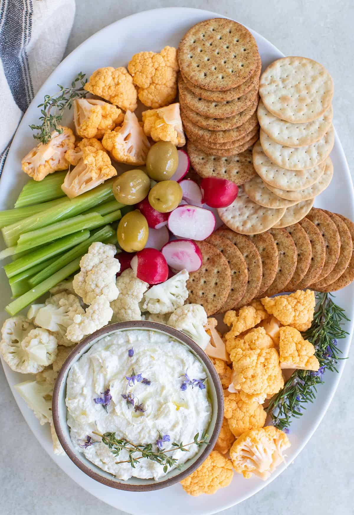 Whipped goat cheese appetizer on a platter with fresh vegetables, crackers and olives.