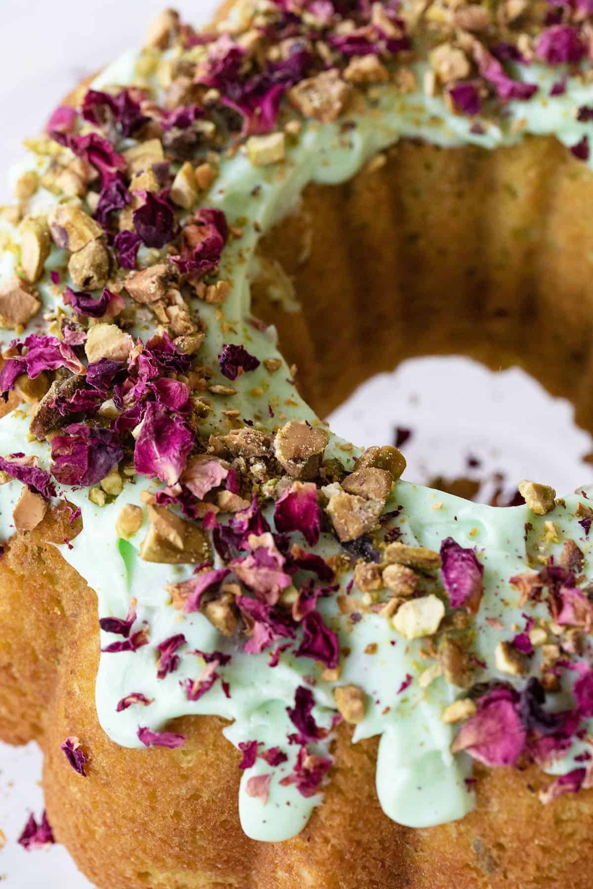 Pistachio bundt cake with green frosting and edible rose petals.