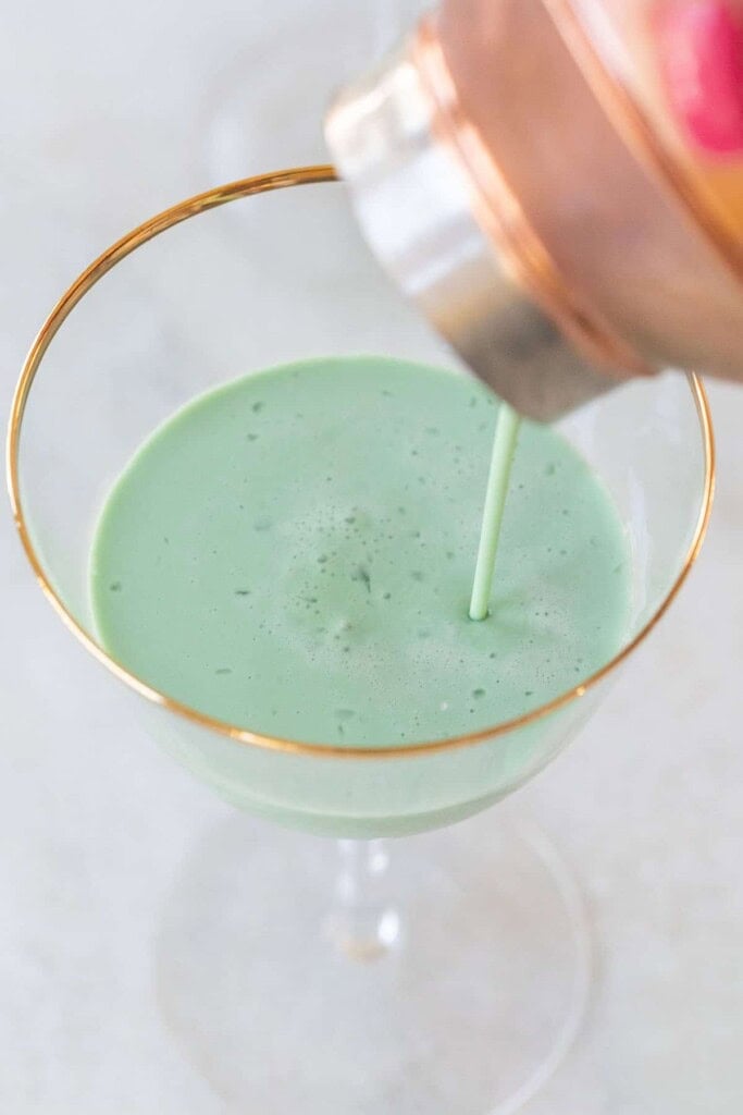 Straining a grasshopper cocktail into a coupe glass.