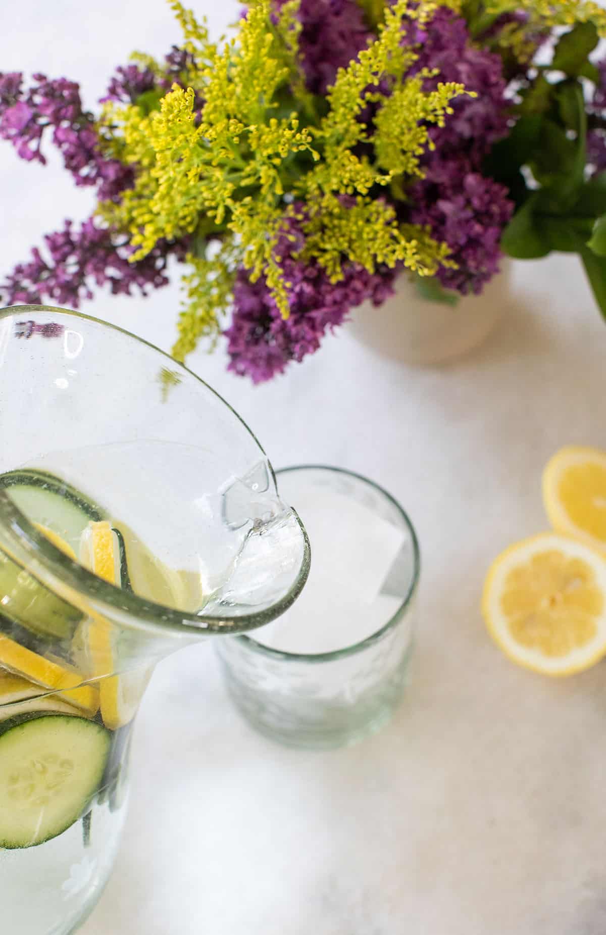 Pouring lemon cucumber water into a glass with ice.