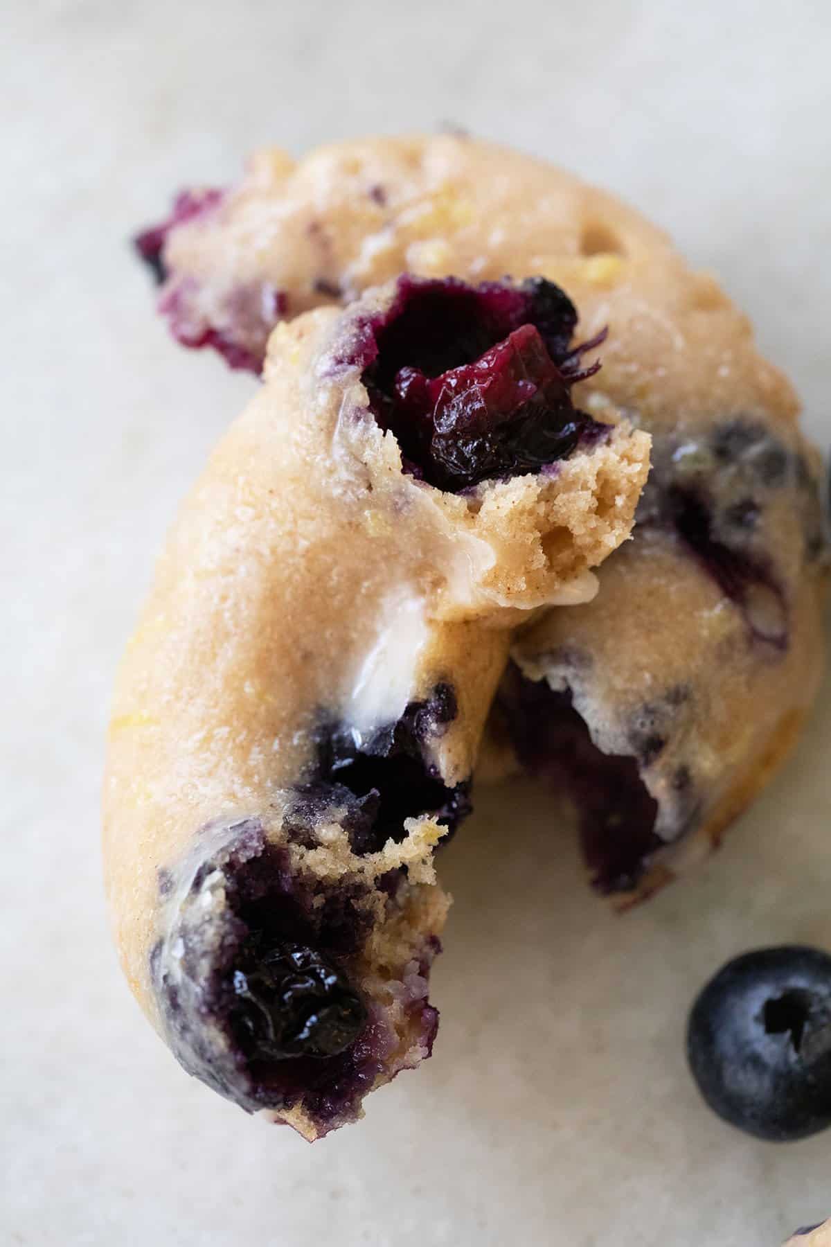 Baked blueberry donut cut in half with juicy blueberries coming out. 