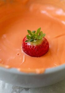 dipping a strawberry into orange candy melts