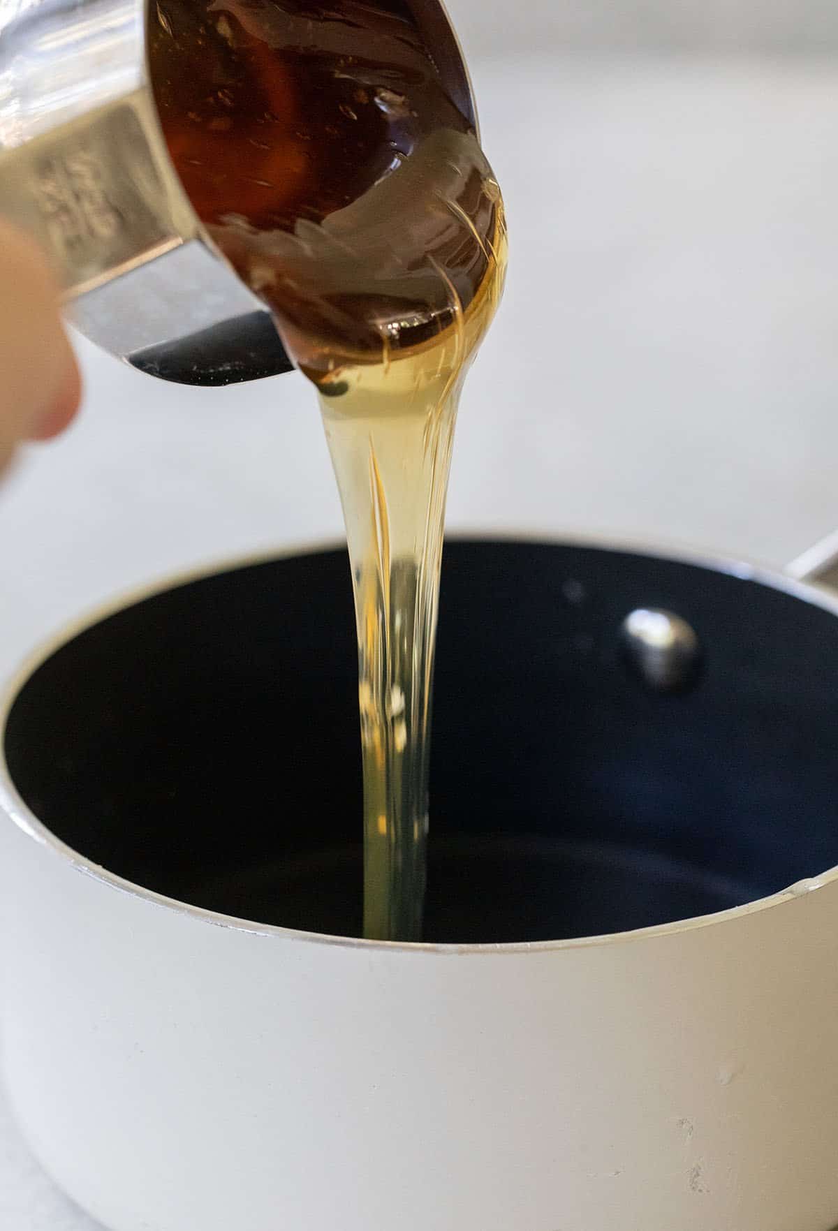 Pouring raw honey into a saucepan to make honey simple syrup.