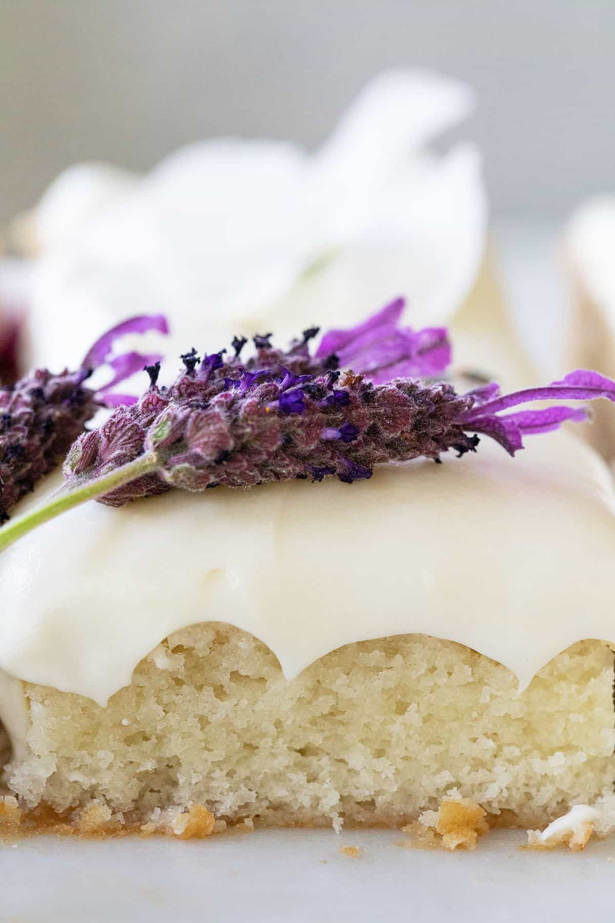 slice of lavender cake with lavender frosting dripping down the side and a slice of lavender over the top