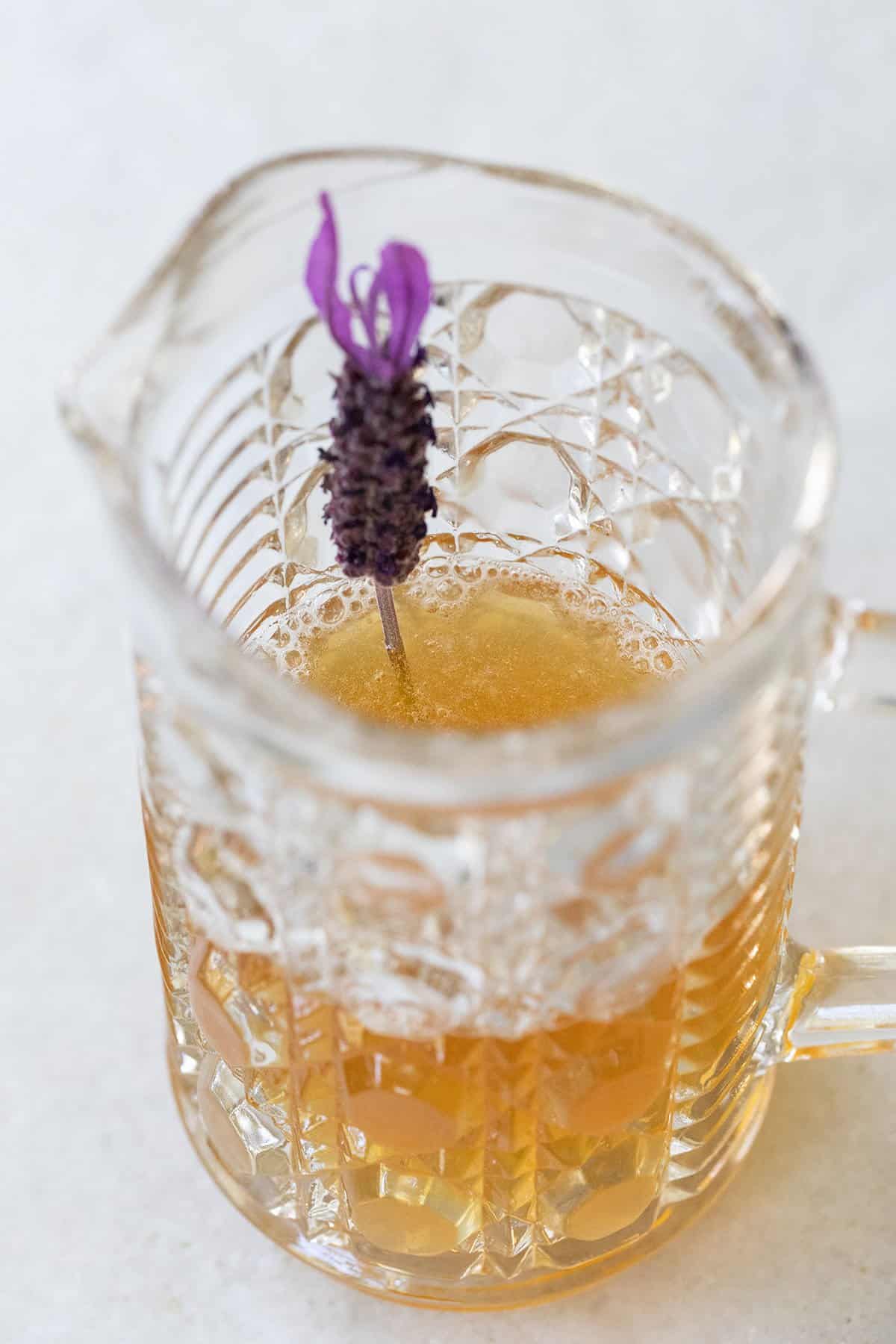 Liquid sweetener in a glass jar made with honey and water and garnished with lavender. 