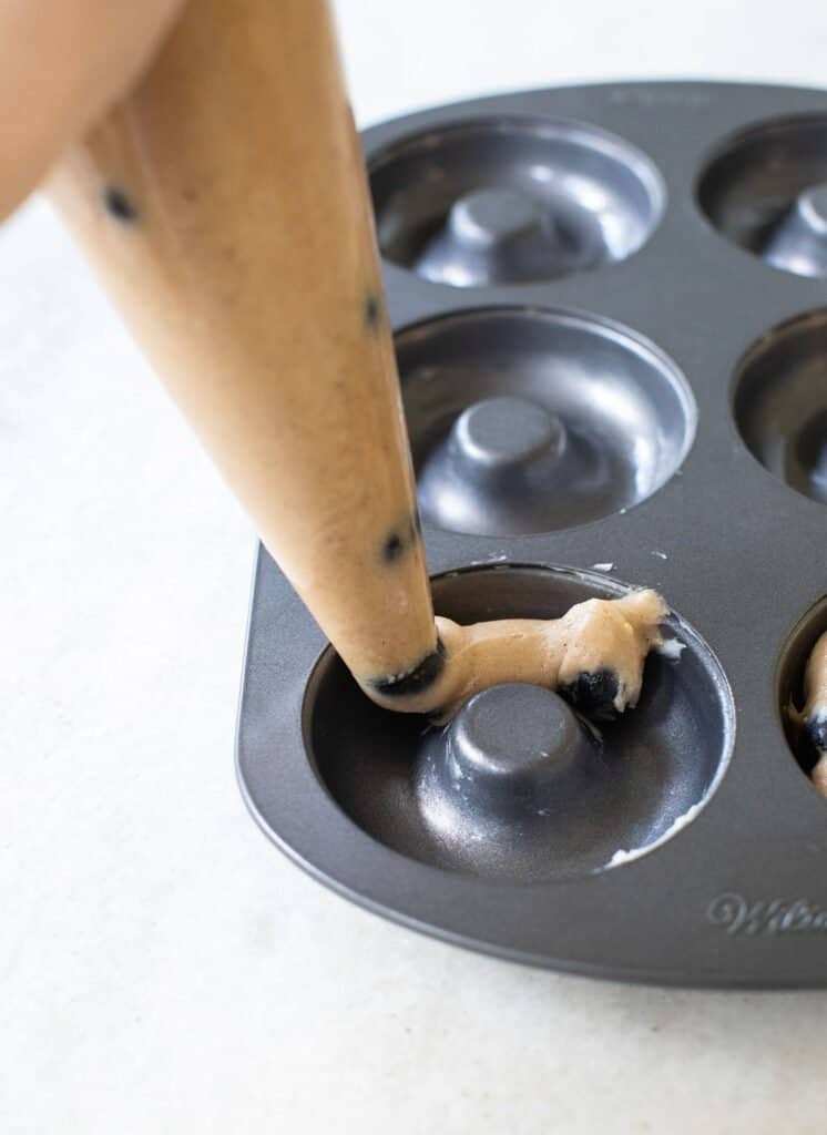 piping blueberry donut batter into a donut pan.