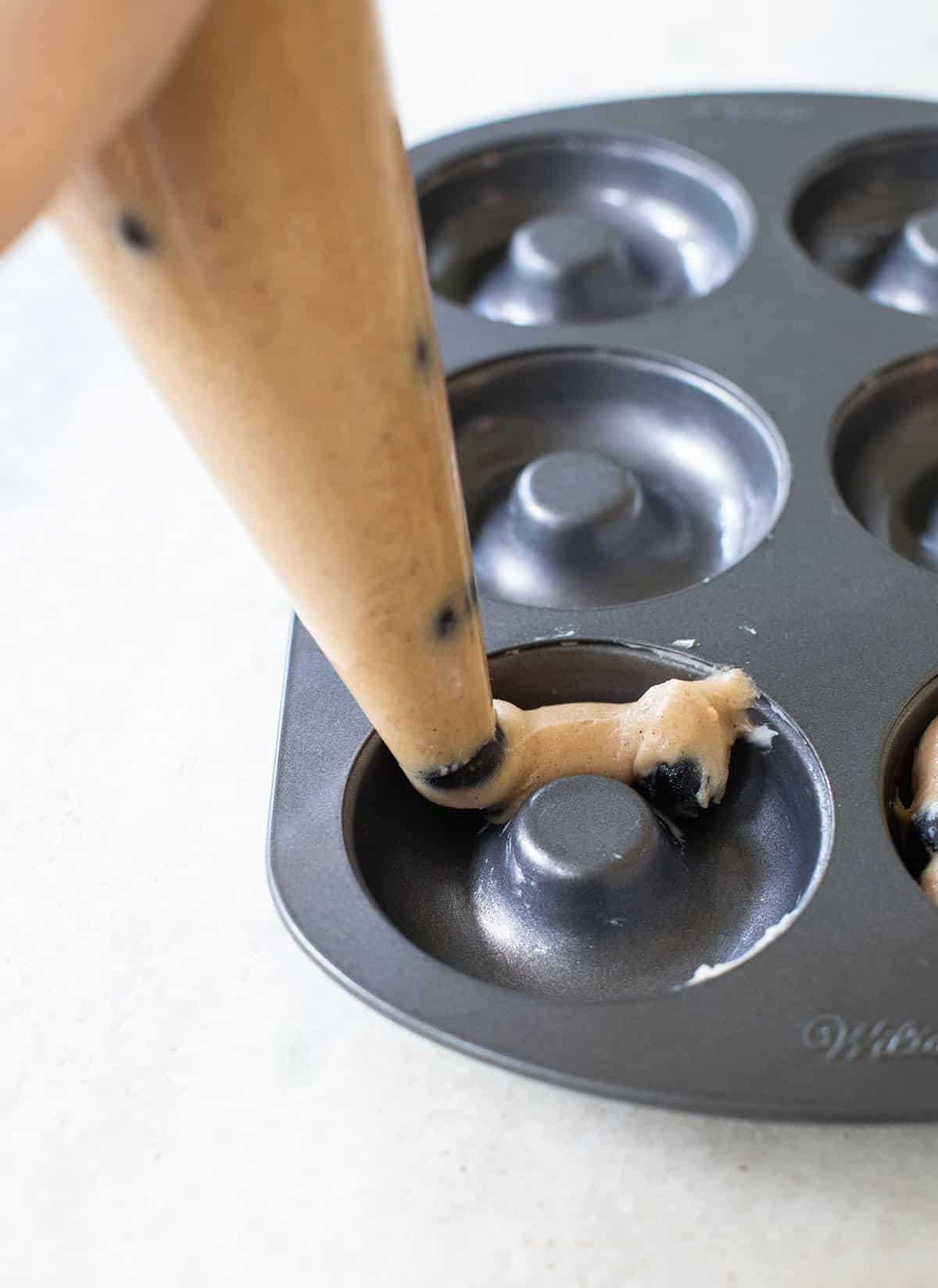 piping donut batter into a donut pan