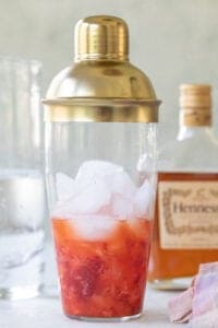 strawberry, lime juice and Hennessy in a clear cocktail shaker