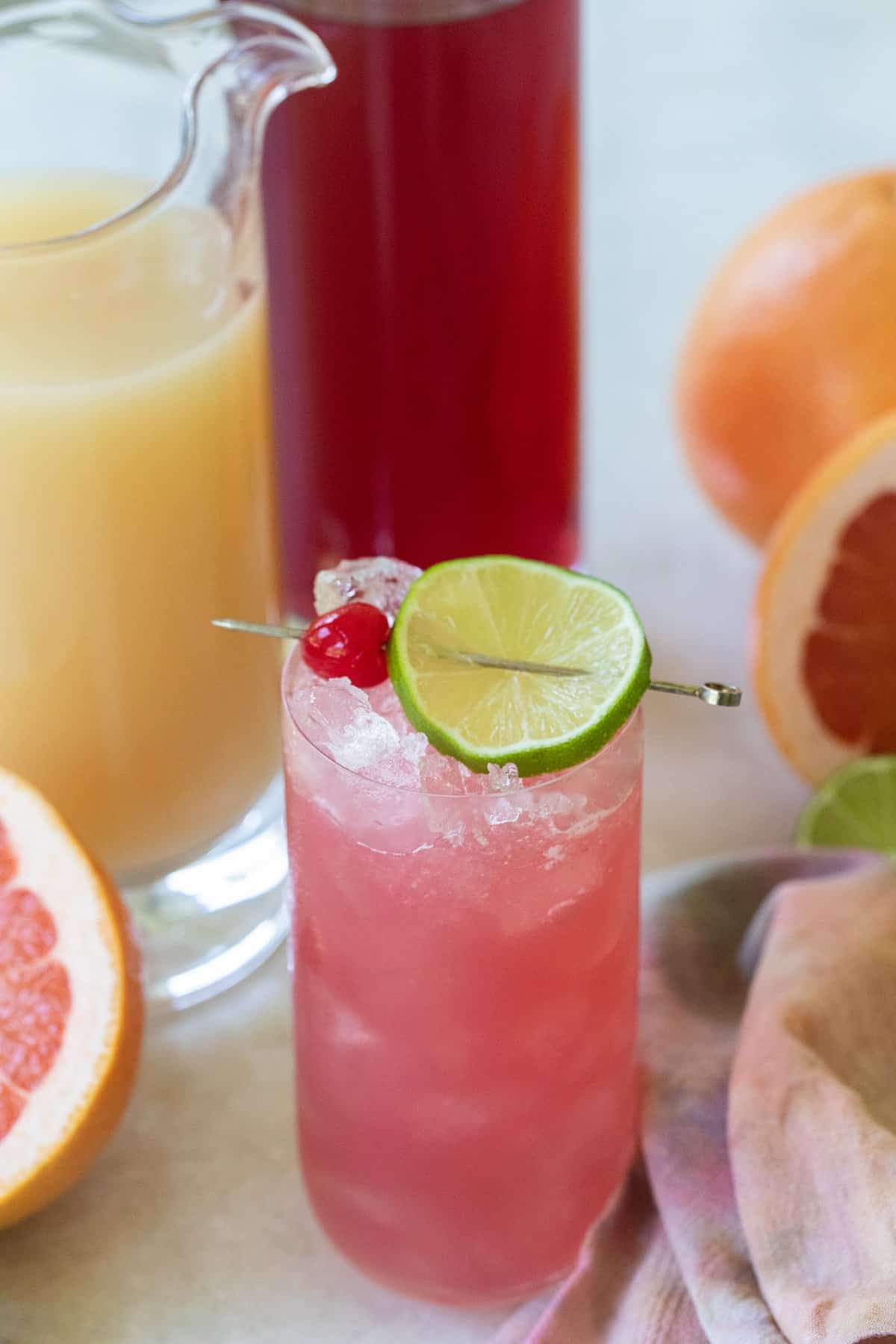 Pink sea breeze cocktail in tall glass with ice, lime and cherries. 