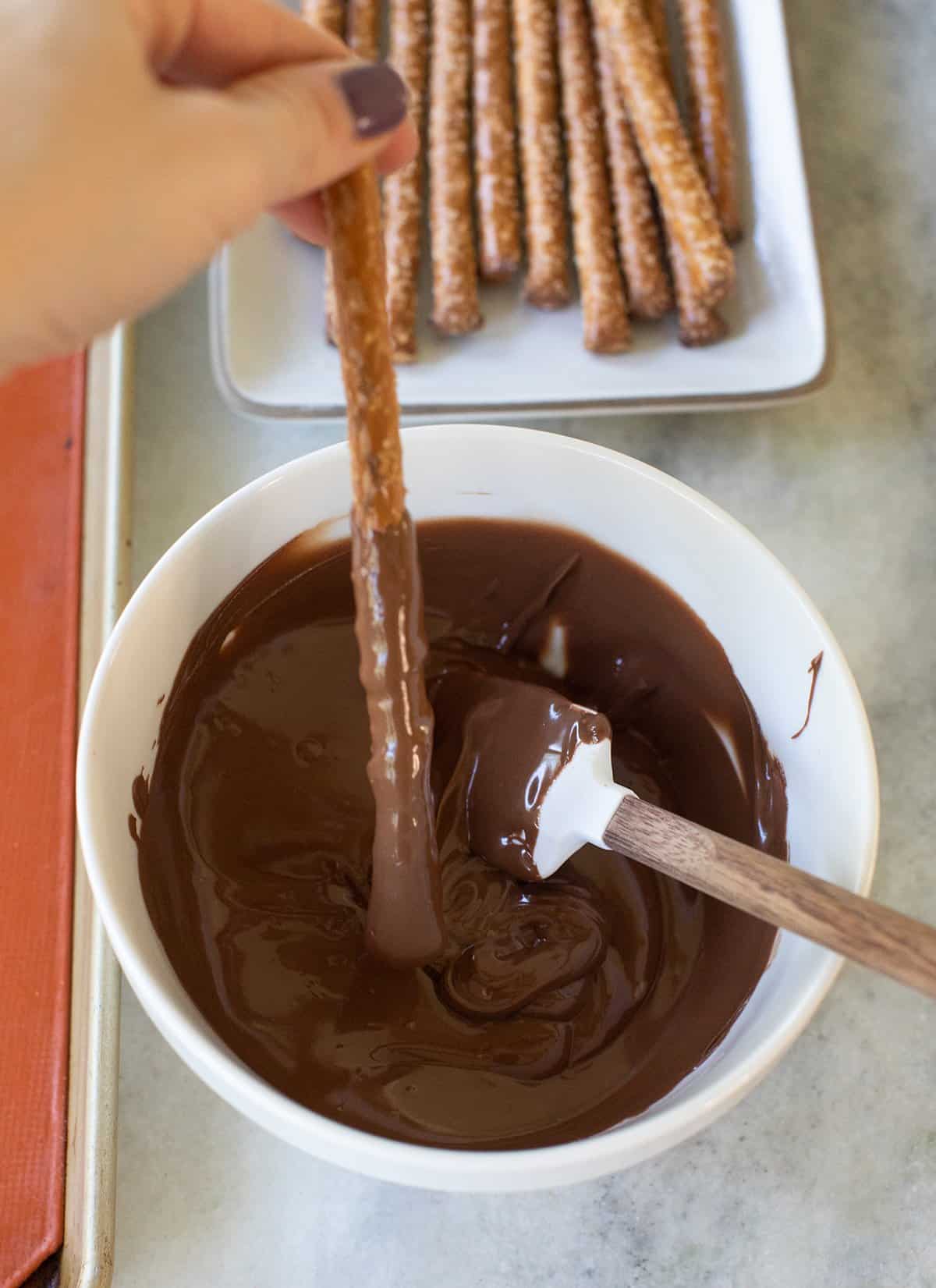 dipping a pretzel rod into melted chocolate 